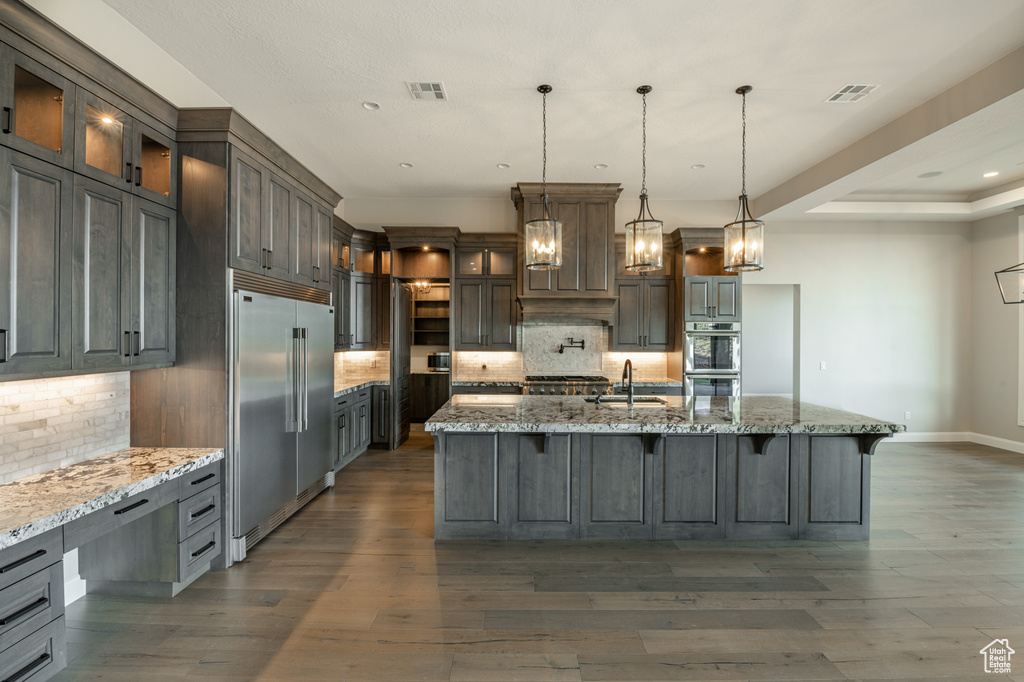 Kitchen with stainless steel appliances, sink, backsplash, a large island, and dark wood-type flooring