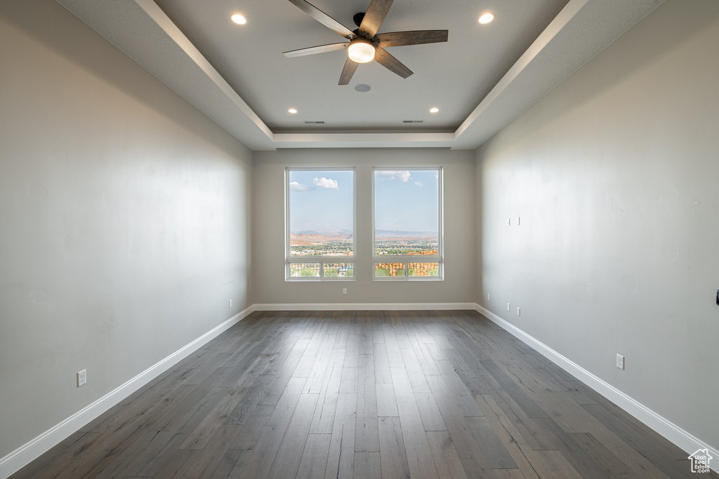 Empty room with ceiling fan, dark hardwood / wood-style floors, and a tray ceiling