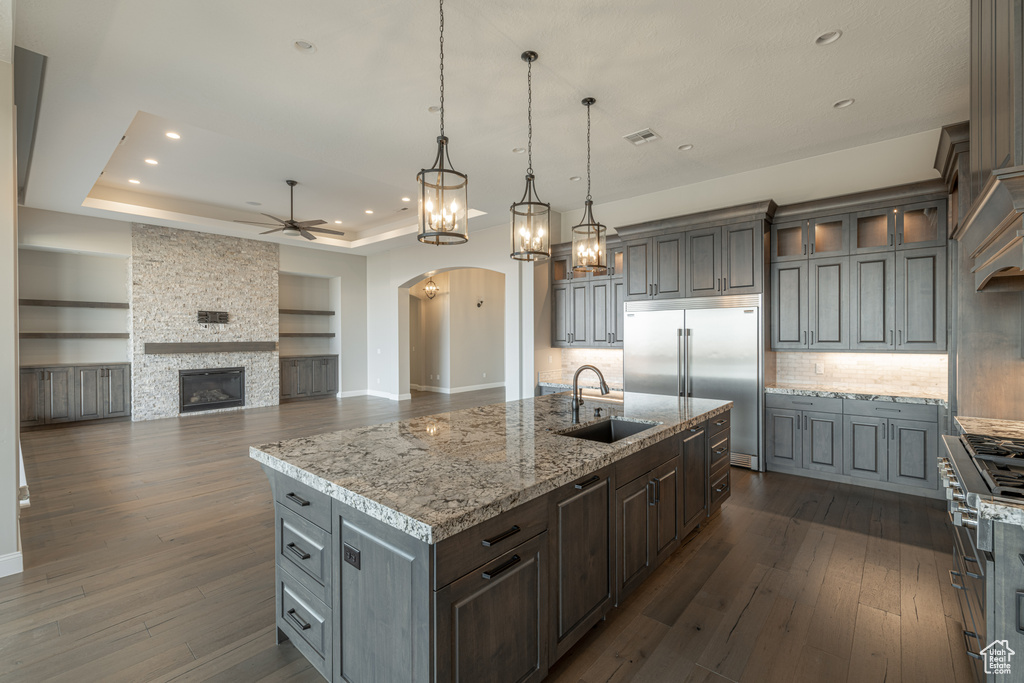 Kitchen with backsplash, dark hardwood / wood-style flooring, a tray ceiling, a fireplace, and sink