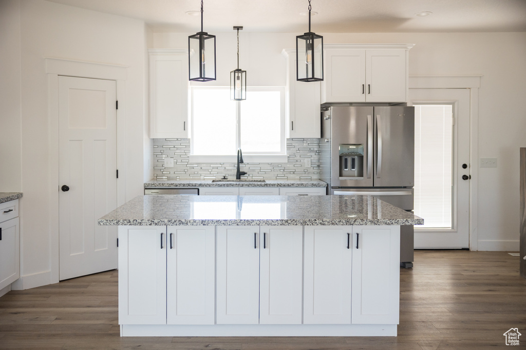 Kitchen with stainless steel fridge, decorative backsplash, white cabinetry, a center island, and pendant lighting