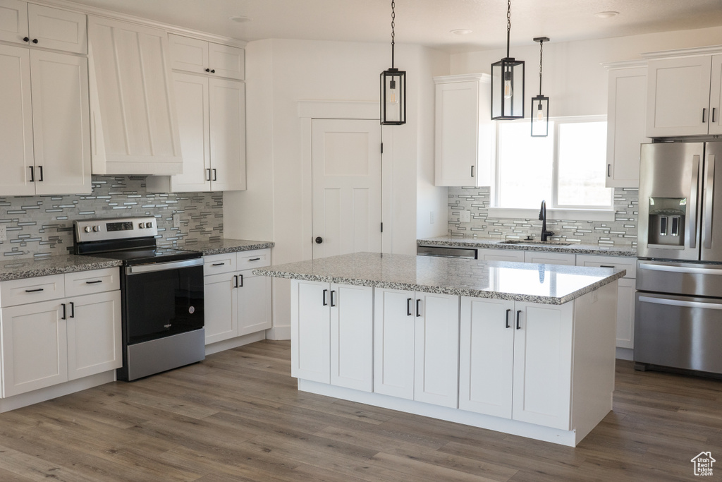 Kitchen featuring appliances with stainless steel finishes, decorative backsplash, a kitchen island, white cabinetry, and wood finished floors