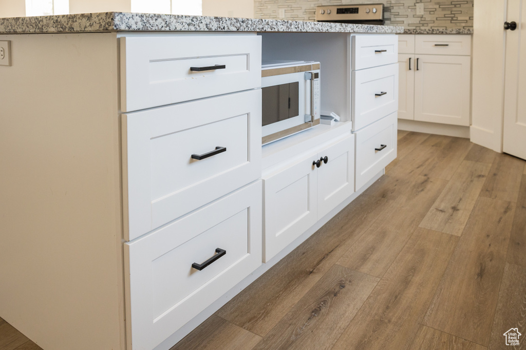 Kitchen view of white microwave, light wood-style floors, white cabinets, decorative backsplash, and light stone counters