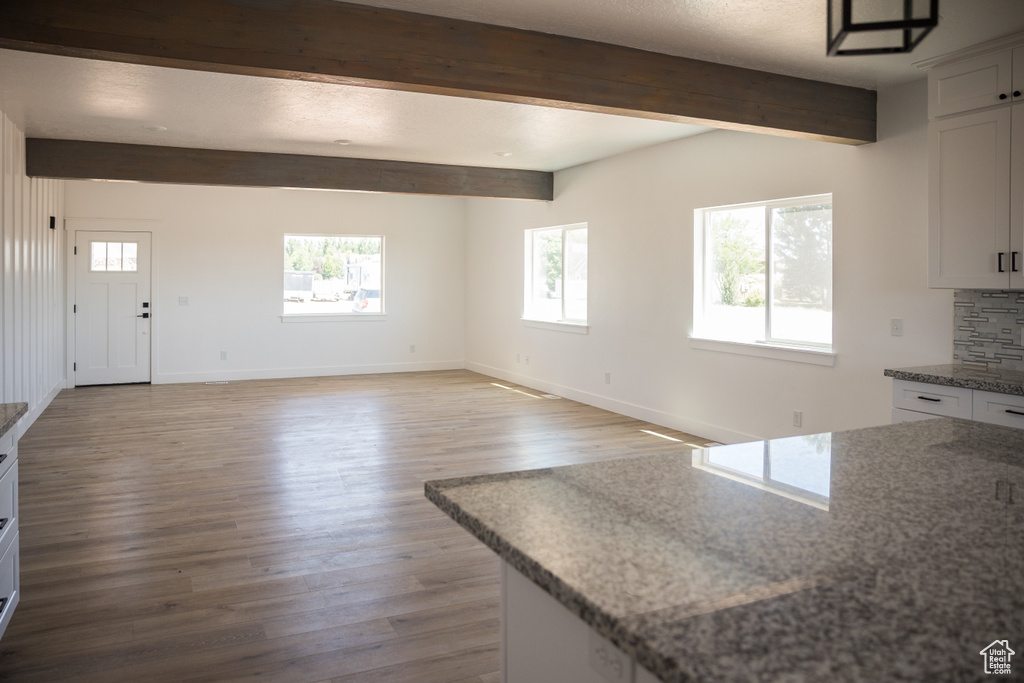 Kitchen featuring beamed ceiling, wood finished floors, light stone countertops, white cabinets, and backsplash
