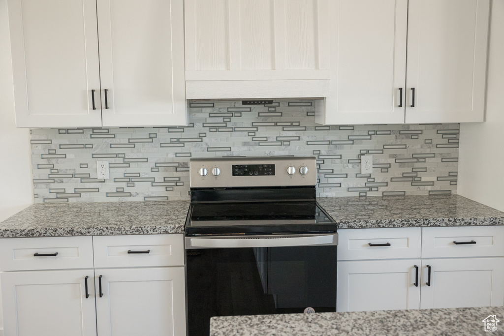 Kitchen featuring electric stove, white cabinets, and backsplash
