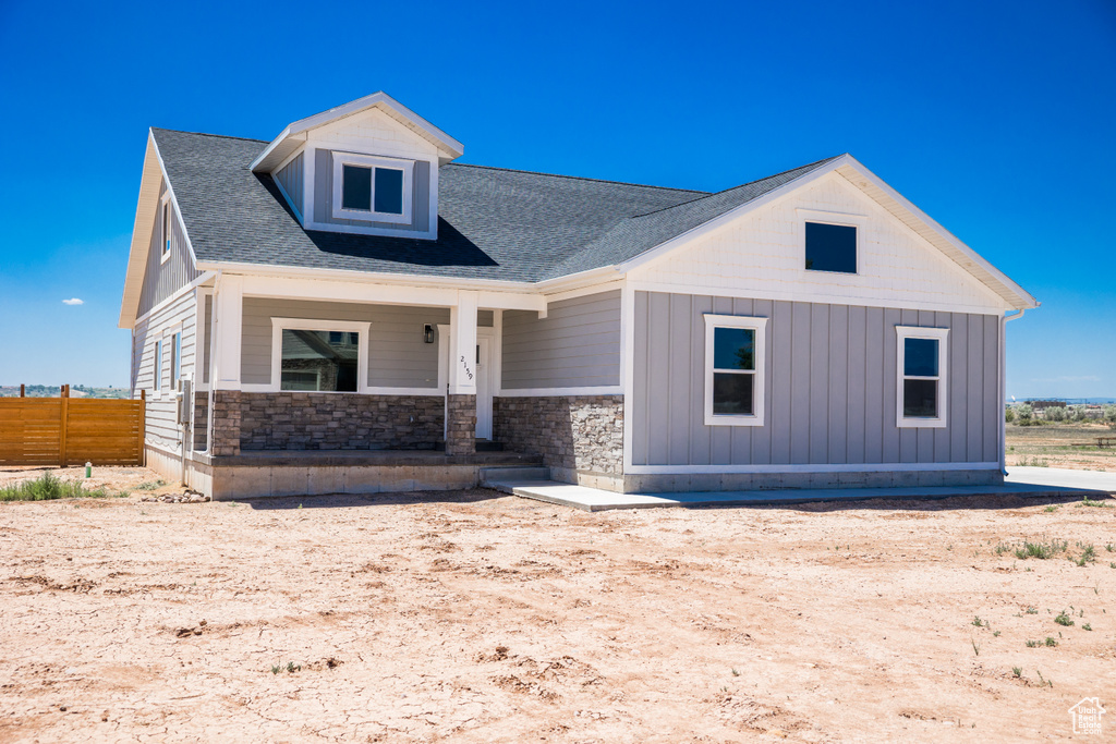 View of front of home with covered porch, stone siding, board and batten siding, and a shingled roof