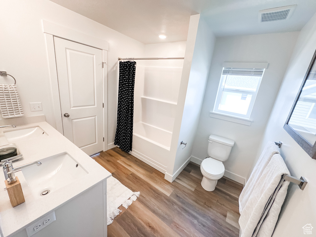 Full bathroom featuring toilet, wood-type flooring, shower / bath combo, and double vanity