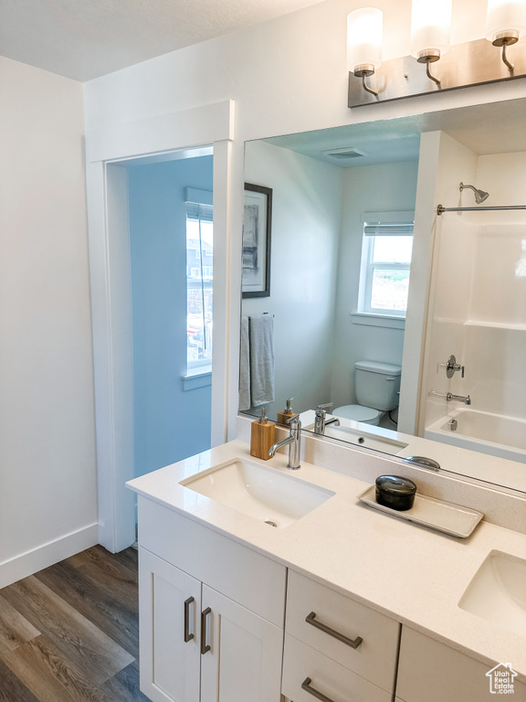 Full bathroom with shower / tub combination, dual vanity, wood-type flooring, and toilet