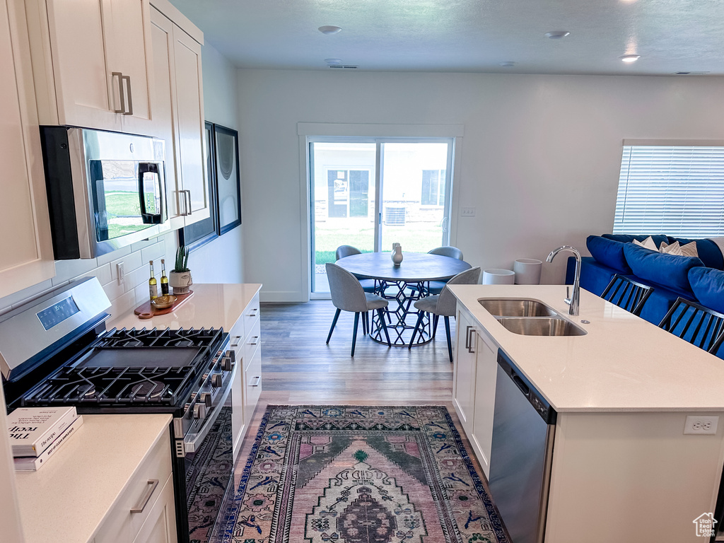Kitchen with white cabinets, sink, a center island with sink, appliances with stainless steel finishes, and light hardwood / wood-style flooring