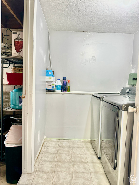 Laundry room featuring washing machine and clothes dryer, light tile patterned floors, and a textured ceiling
