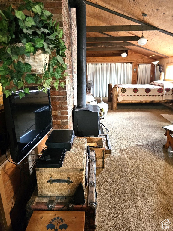 Bedroom with a wood stove, multiple windows, lofted ceiling, and carpet floors