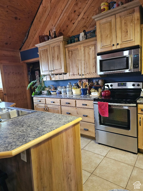 Kitchen featuring light tile patterned flooring, wooden walls, stainless steel appliances, and vaulted ceiling