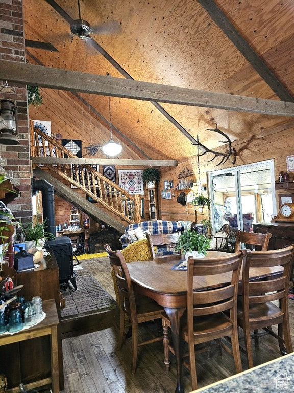 Dining area with wooden walls, hardwood / wood-style flooring, brick wall, vaulted ceiling with beams, and a wood stove