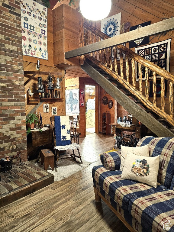 Living room featuring hardwood / wood-style floors, wood walls, brick wall, and a high ceiling