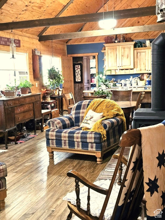 Living room featuring wood walls, vaulted ceiling with beams, light hardwood / wood-style floors, and a wood stove