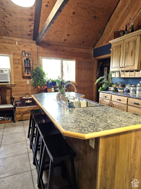 Kitchen featuring lofted ceiling, an island with sink, wooden walls, sink, and light tile patterned flooring