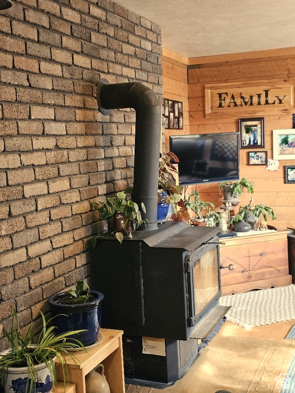 Living room featuring a textured ceiling, wooden walls, brick wall, and a wood stove