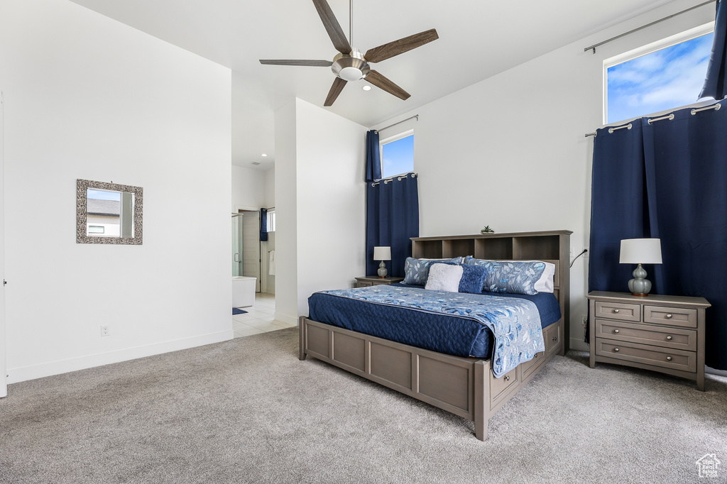 Bedroom featuring light carpet, connected bathroom, multiple windows, and ceiling fan