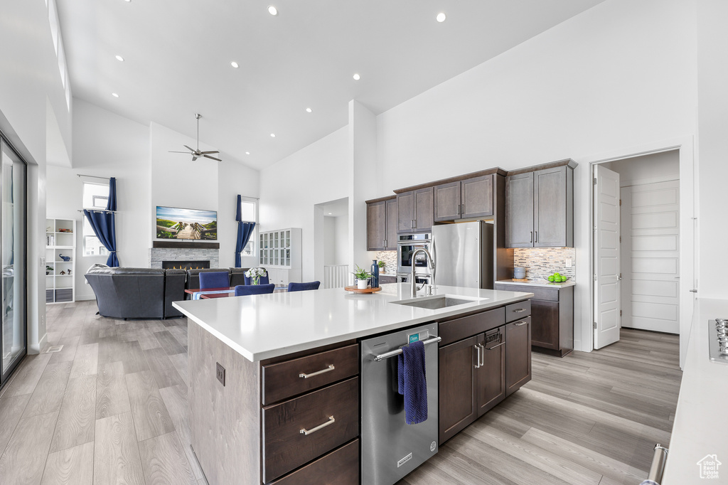 Kitchen with a kitchen island with sink, light hardwood / wood-style flooring, high vaulted ceiling, and stainless steel appliances