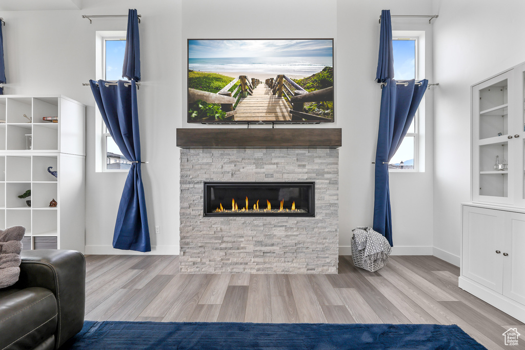 Living room with built in features, a stone fireplace, light hardwood / wood-style flooring, and a wealth of natural light