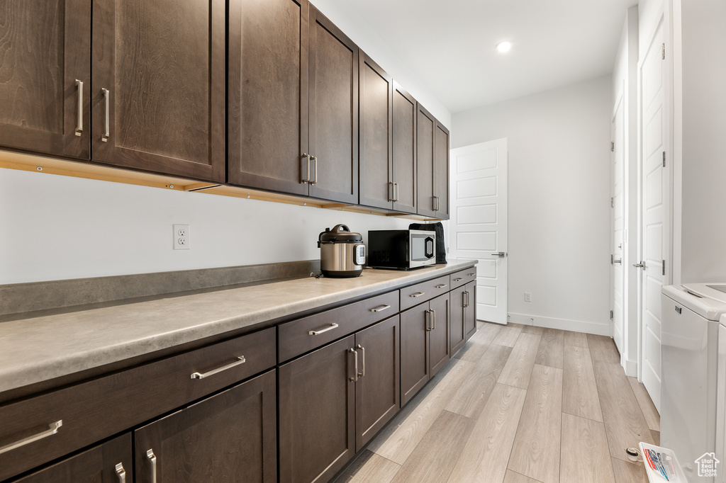 Kitchen with washer / dryer, light hardwood / wood-style flooring, and dark brown cabinets