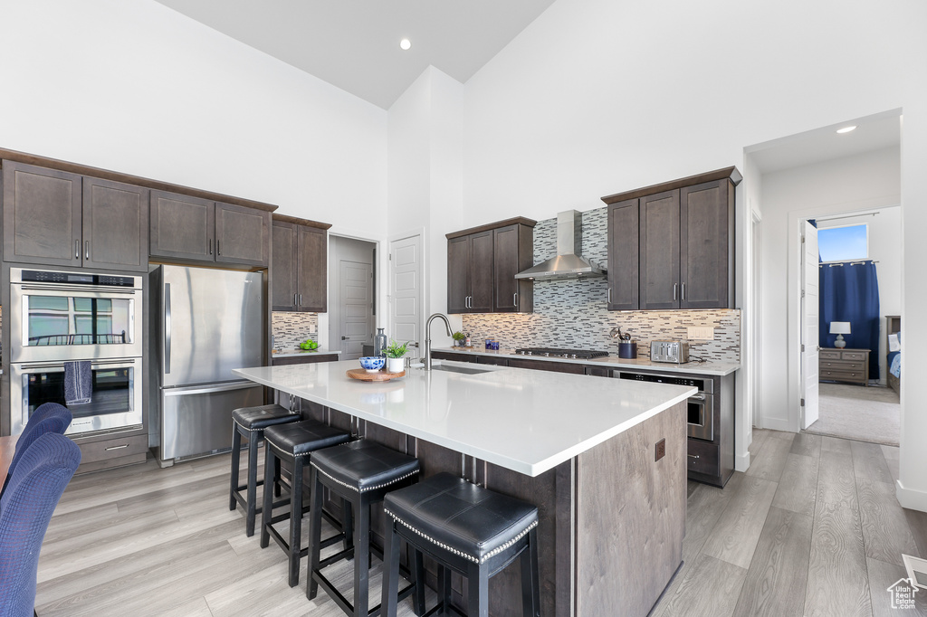 Kitchen with wall chimney range hood, sink, stainless steel appliances, and a kitchen island with sink