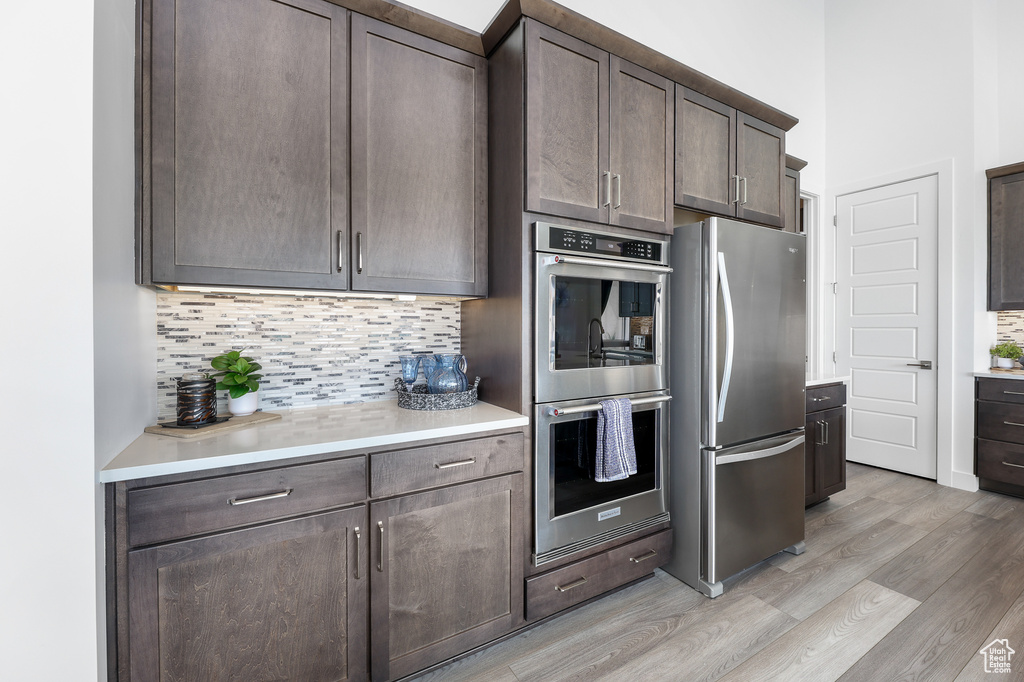 Kitchen featuring light hardwood / wood-style floors, dark brown cabinetry, decorative backsplash, and stainless steel appliances