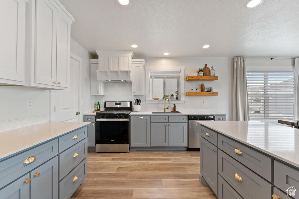 Kitchen with white cabinets, stainless steel appliances, light hardwood / wood-style flooring, and sink