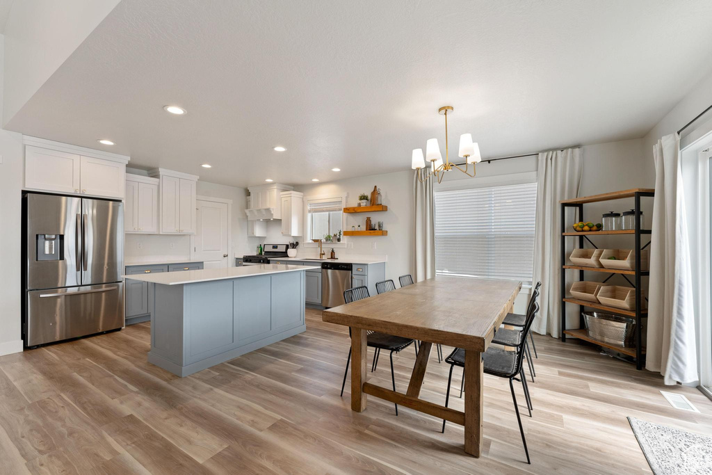 Kitchen with stainless steel appliances, gray cabinetry, white cabinets, light hardwood / wood-style floors, and a kitchen island