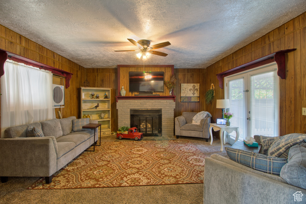 Carpeted living room with wood walls, a fireplace, a textured ceiling, and ceiling fan