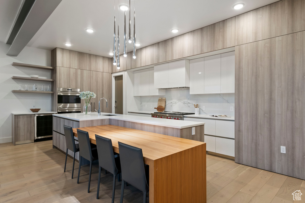 Kitchen with a center island with sink, light wood-type flooring, and beverage cooler