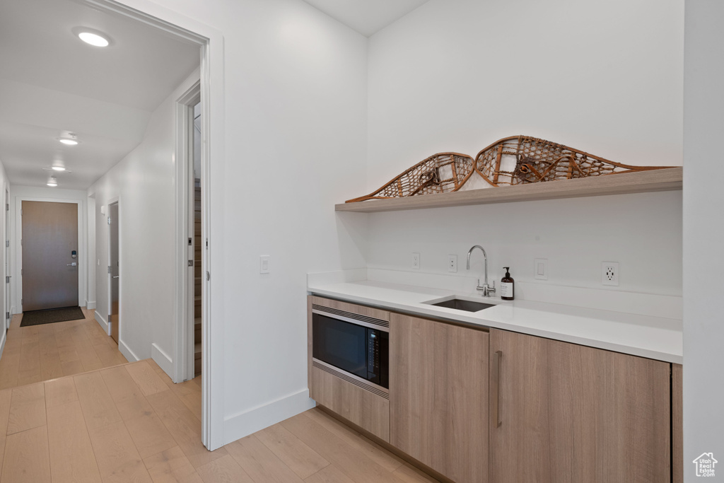 Kitchen with light brown cabinetry, light hardwood / wood-style flooring, sink, and black microwave