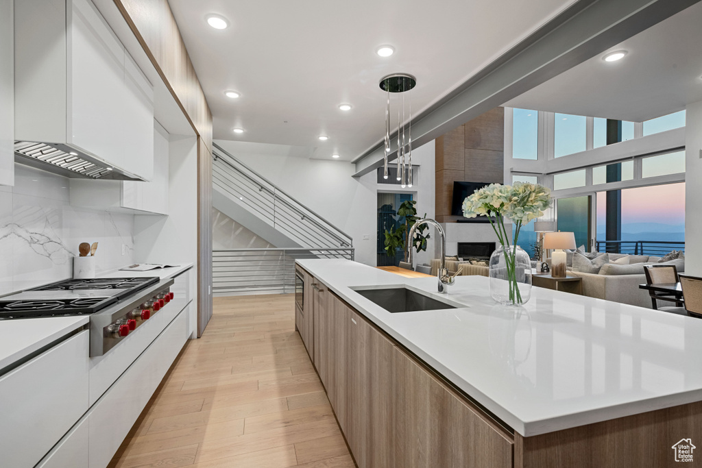 Kitchen with light hardwood / wood-style flooring, a center island with sink, white cabinets, pendant lighting, and sink