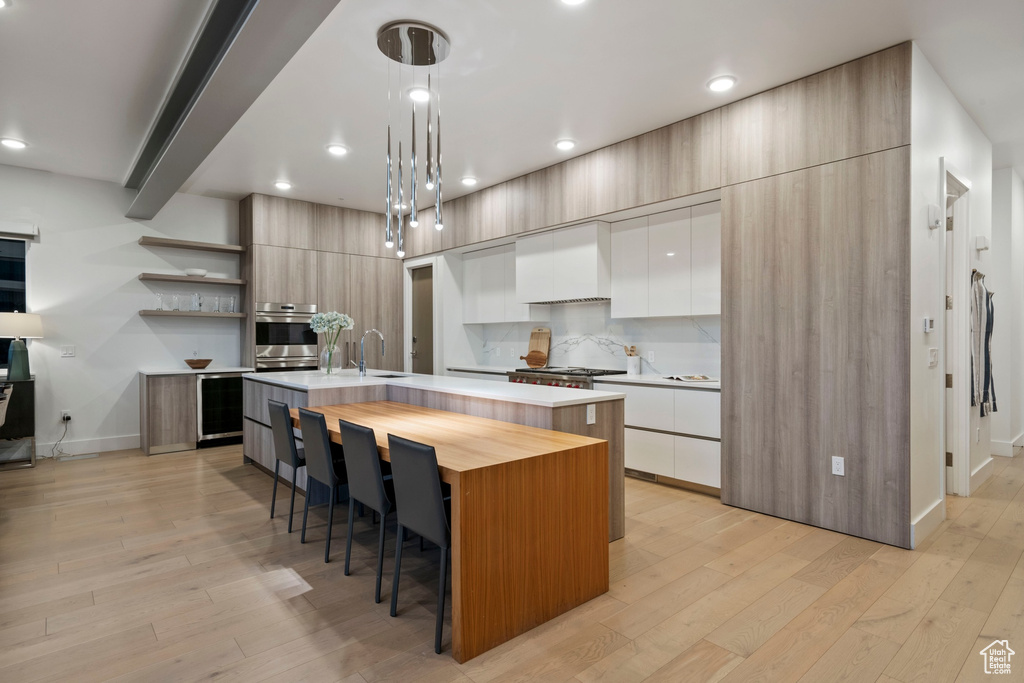 Kitchen featuring a center island with sink, pendant lighting, light hardwood / wood-style floors, stainless steel oven, and custom exhaust hood