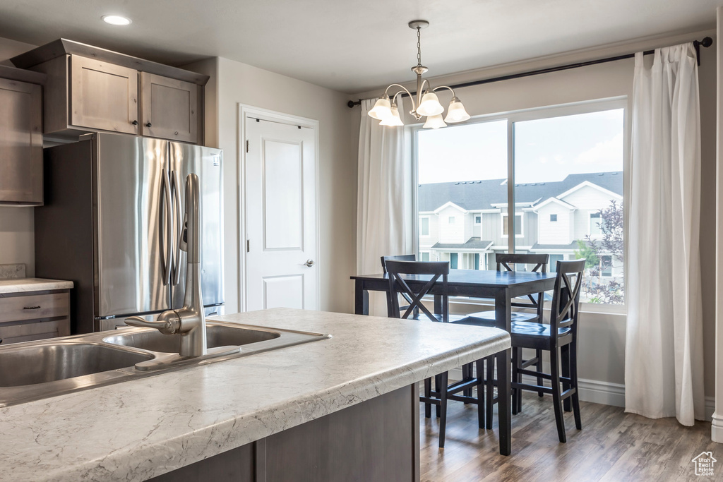 Kitchen with a notable chandelier, hardwood / wood-style flooring, hanging light fixtures, sink, and stainless steel fridge