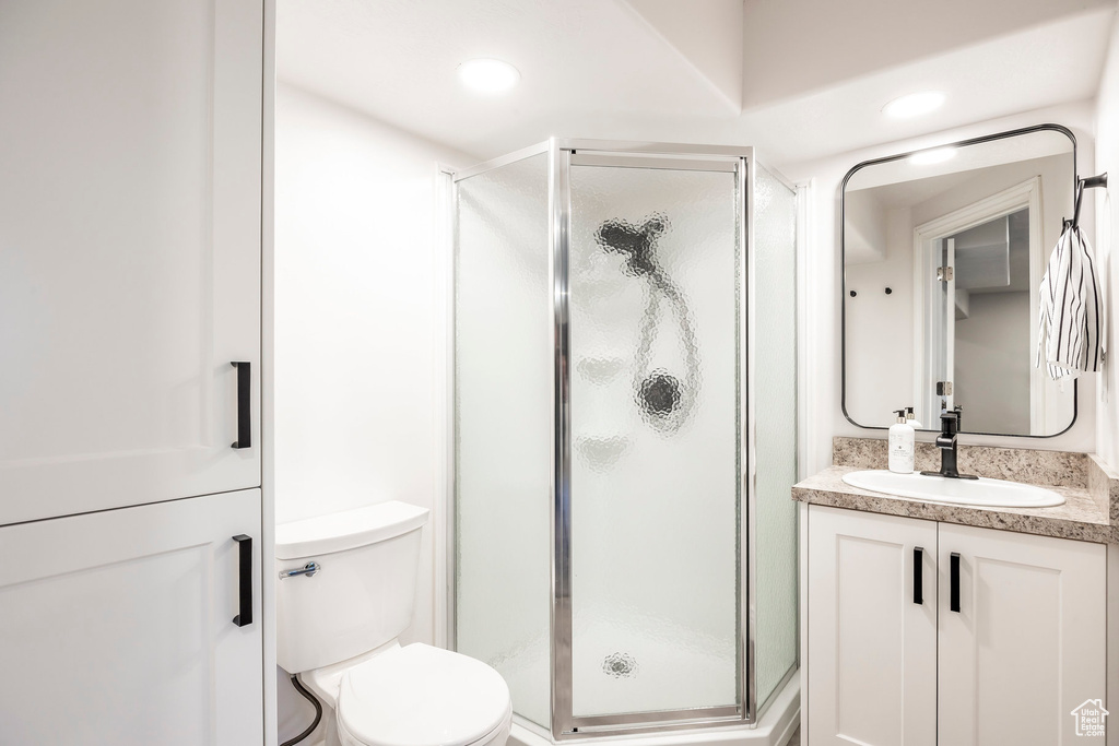 Bathroom featuring a shower with door, toilet, and vanity