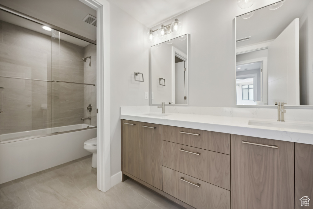 Full bathroom featuring toilet, tiled shower / bath, tile patterned flooring, and double sink vanity