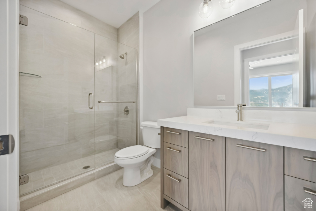 Bathroom with a shower with shower door, vanity, tile patterned flooring, and toilet