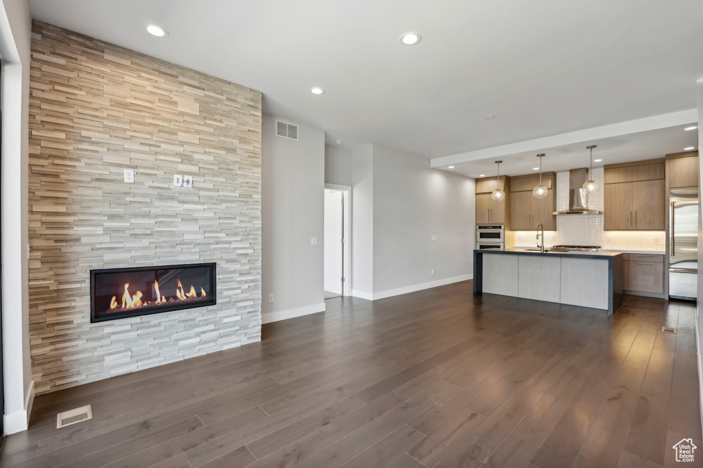 Unfurnished living room with a tile fireplace, sink, and dark hardwood / wood-style floors