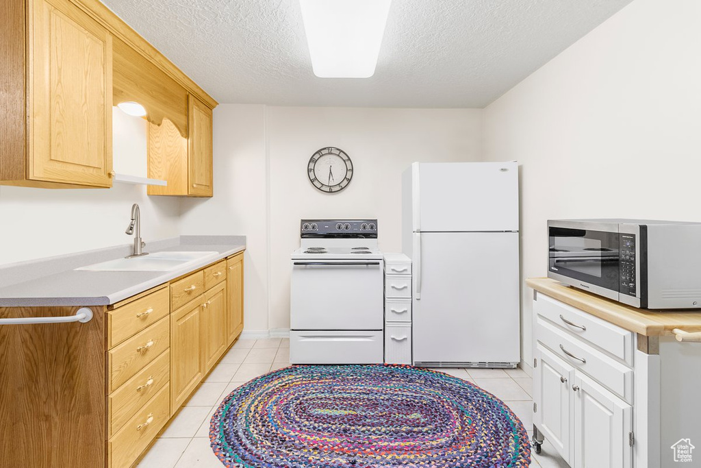 Kitchen with light brown cabinets, white appliances, sink, a textured ceiling, and light tile patterned floors