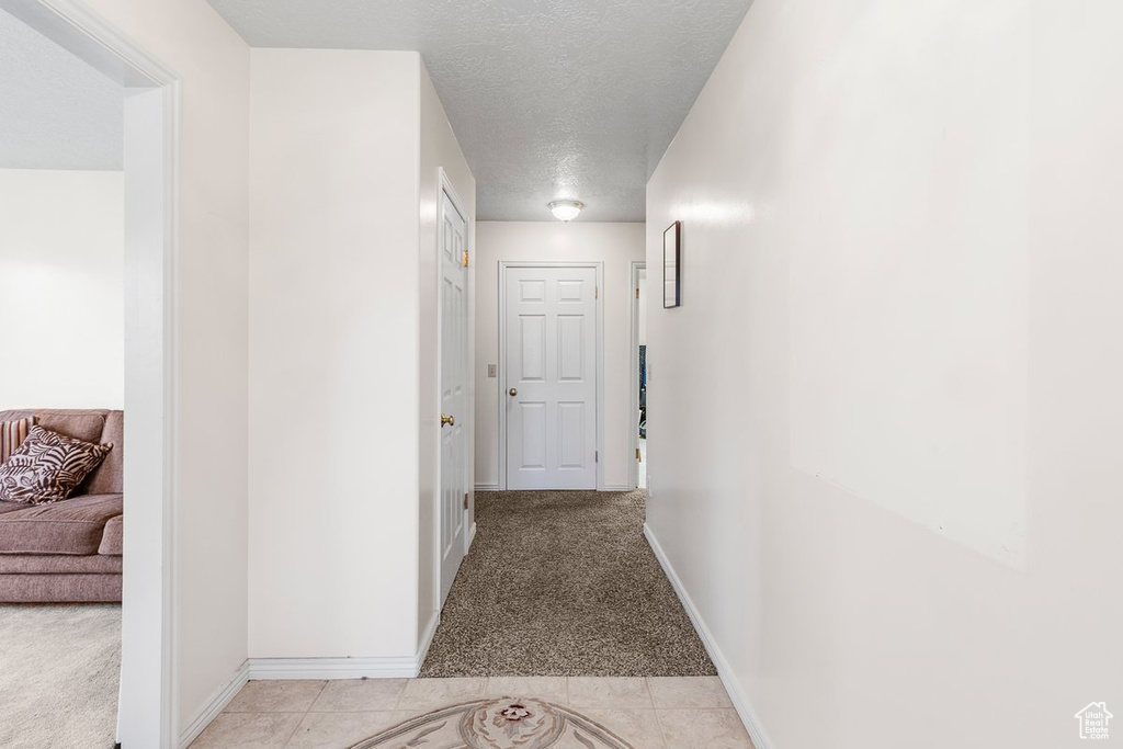 Hallway featuring a textured ceiling and light colored carpet