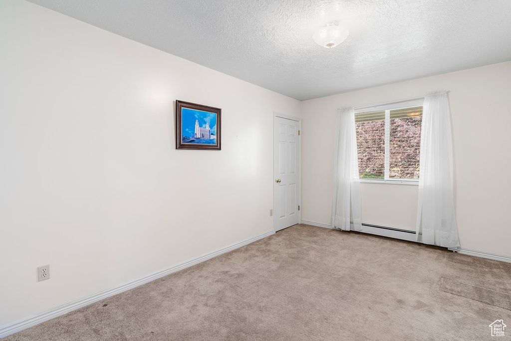 Spare room with a baseboard heating unit, light colored carpet, and a textured ceiling