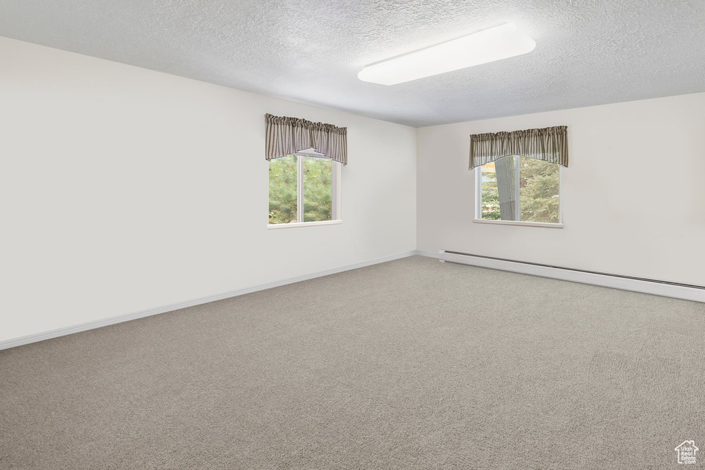 Carpeted empty room featuring a textured ceiling and a baseboard heating unit