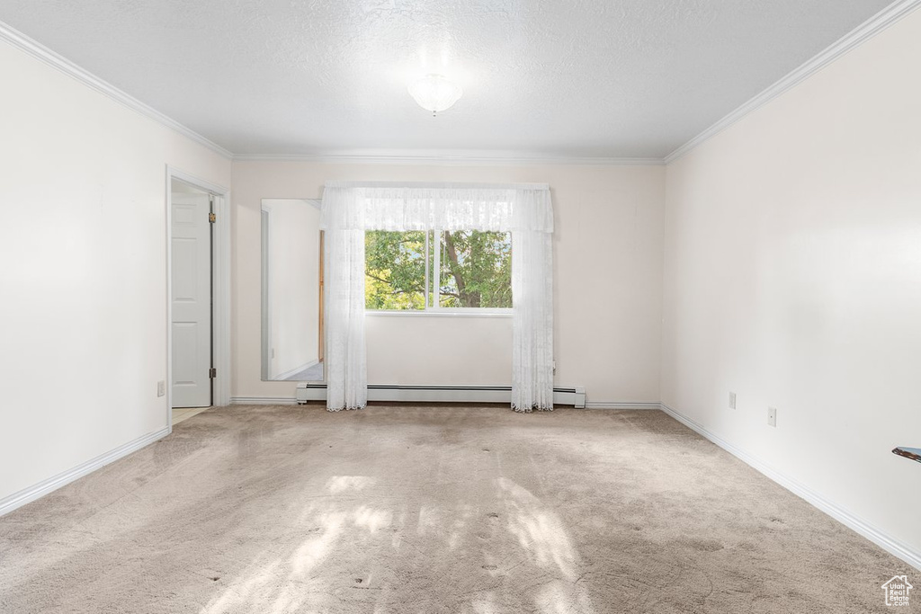 Carpeted spare room with a baseboard heating unit, a textured ceiling, and crown molding