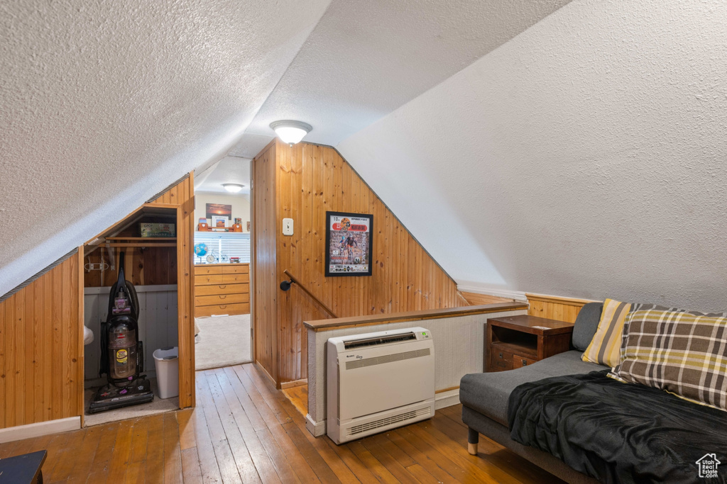 Sitting room with vaulted ceiling, a textured ceiling, wooden walls, and hardwood / wood-style floors