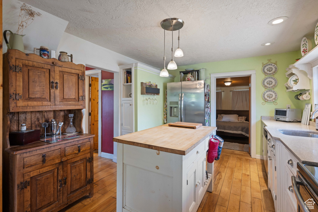 Kitchen with wood counters, light wood-type flooring, stainless steel fridge with ice dispenser, a center island, and white cabinetry