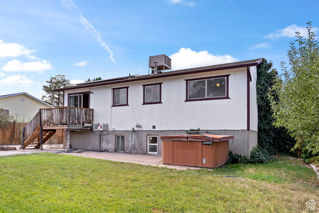 Rear view of property featuring a deck, a hot tub, and a lawn