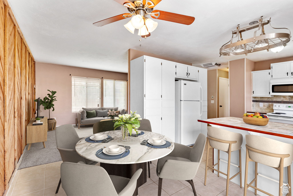 Dining space featuring wooden walls, ceiling fan, and light tile patterned floors