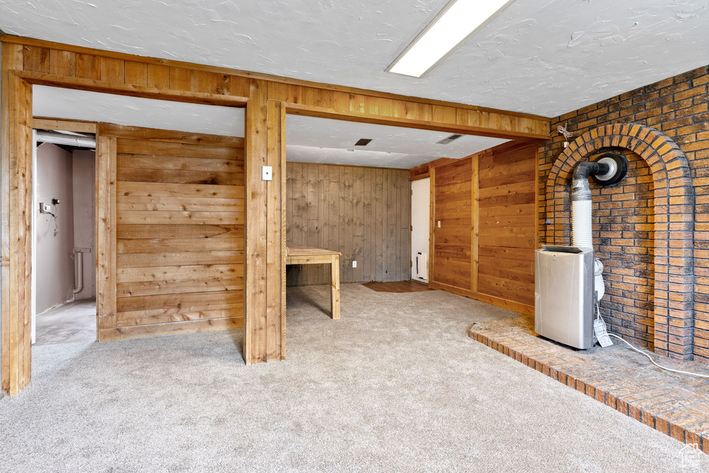 Basement with a wood stove, wooden walls, a textured ceiling, brick wall, and carpet