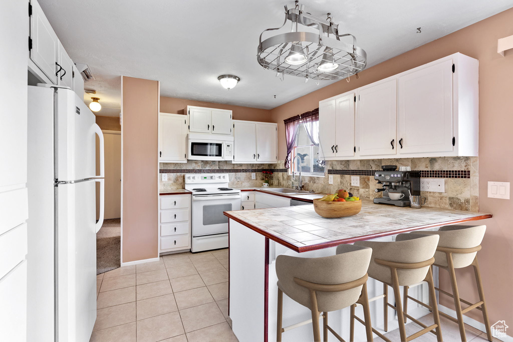 Kitchen featuring white appliances, sink, white cabinets, and kitchen peninsula