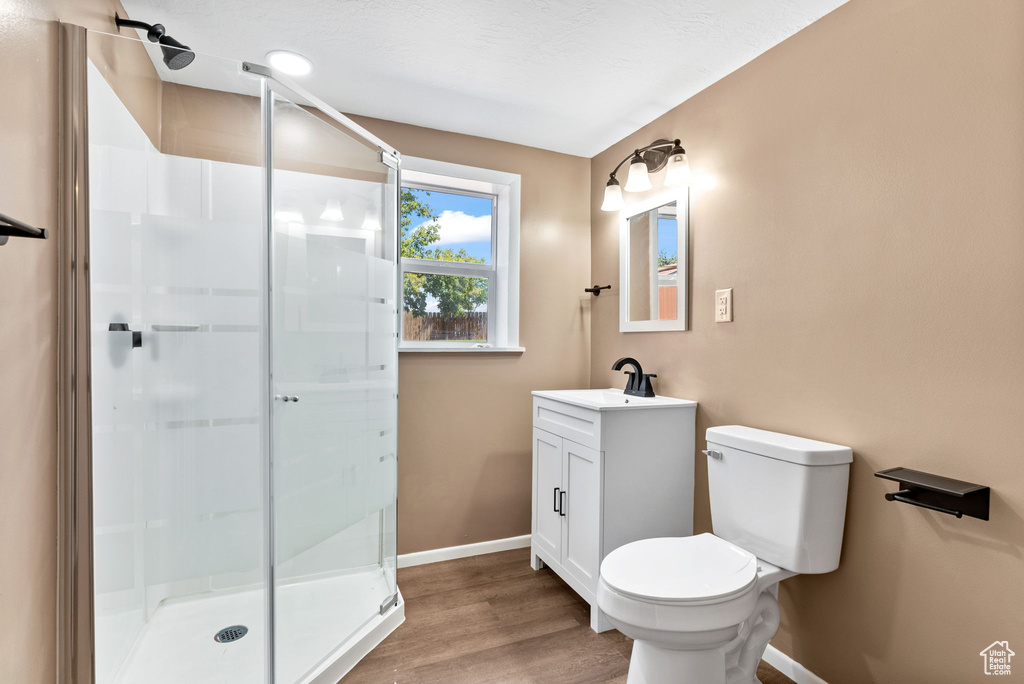 Bathroom with toilet, a shower with door, hardwood / wood-style floors, and vanity